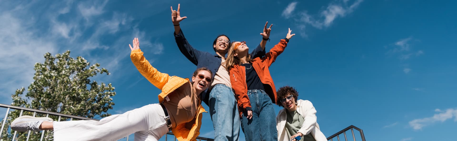 Grupo de amigos ao ar livre, sorrindo com os braços erguidos sob o céu azul